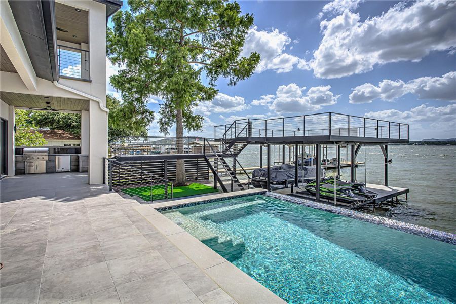 Outdoor pool featuring boat lift, an outdoor kitchen, a dock, stairway, and a water view