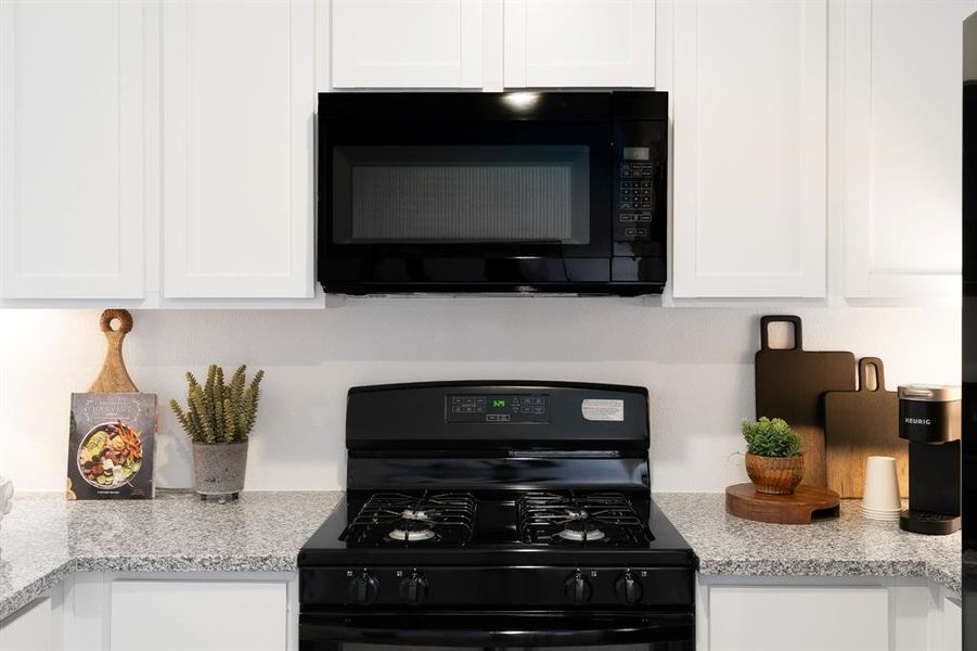 Kitchen featuring black appliances, white cabinets, and light stone countertops