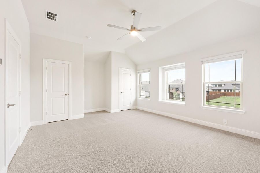 Empty bedroom with vaulted ceiling, ceiling fan, carpet flooring, and three windows with neighborhood views