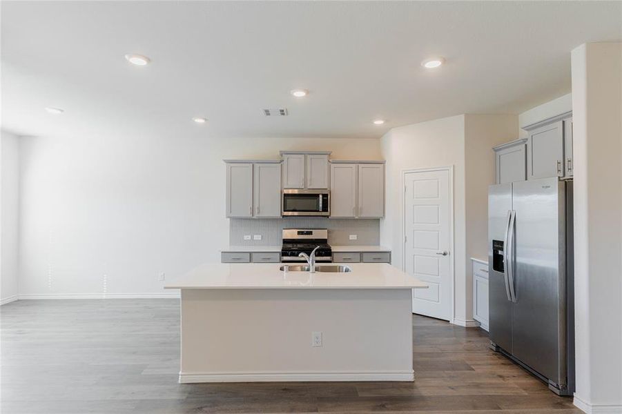 Kitchen with sink, appliances with stainless steel finishes, gray cabinetry, hardwood / wood-style floors, and a center island with sink