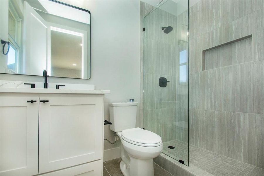 Bathroom with tile patterned flooring, vanity, toilet, and tiled shower