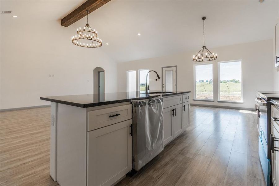 Kitchen with a center island with sink, stainless steel dishwasher, sink, light wood-type flooring, and vaulted ceiling with beams