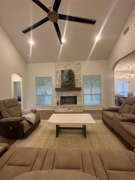 Vaulted ceiling living area featuring a stone fireplace with wood mantel, large windows, recessed lighting, and a ceiling fan