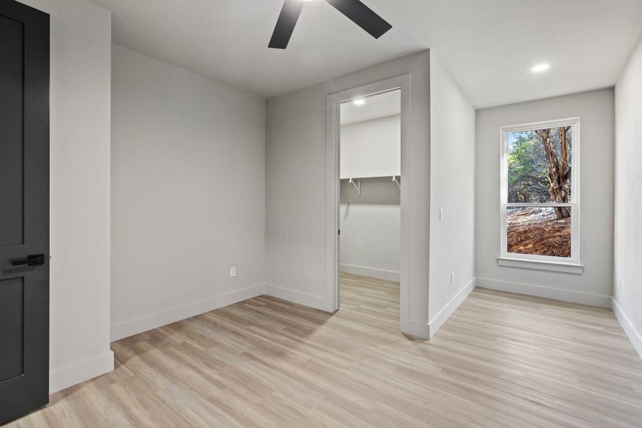 Unfurnished bedroom featuring a ceiling fan, baseboards, recessed lighting, a spacious closet, and light wood-style floors