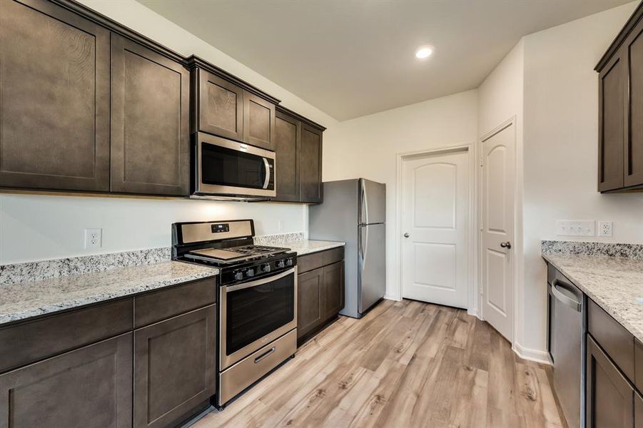 Kitchen with stainless steel appliances, light wood-style floors, light stone counters, and dark cabinets