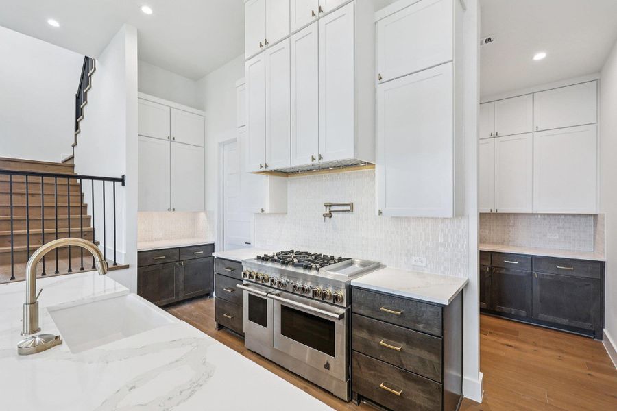 Kitchen with white cabinetry, recessed lighting, range with two ovens, light wood-style floors, and tasteful backsplash