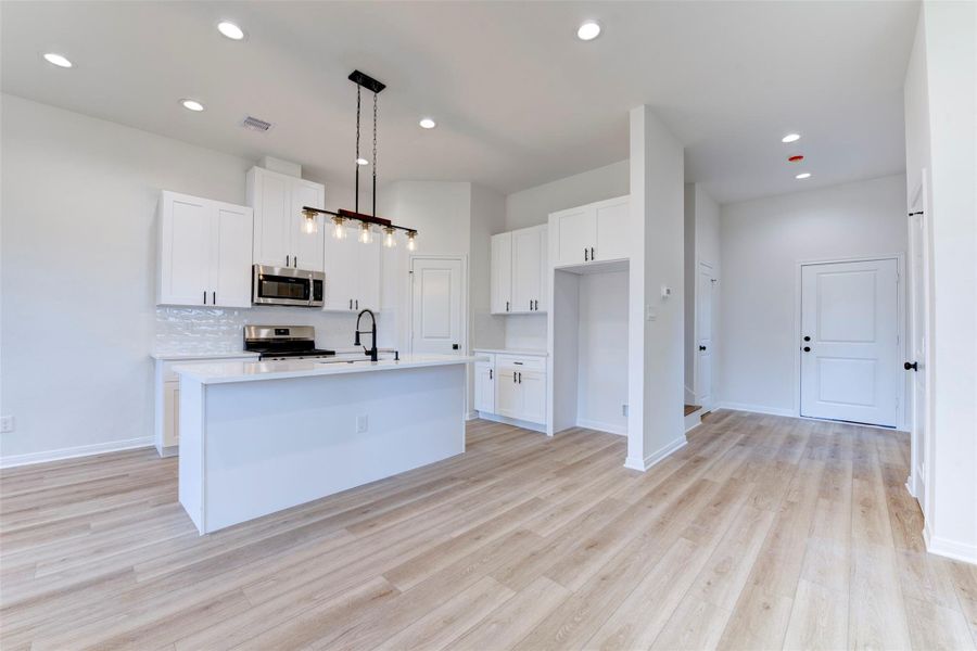 Full view of the clean, modern kitchen with a quartz island, deep single-basin sink, and matte black pull-down faucet. White shaker cabinetry, subway tile backsplash, and stainless appliances keep the look crisp, while pendant lighting adds a warm, elevated touch.