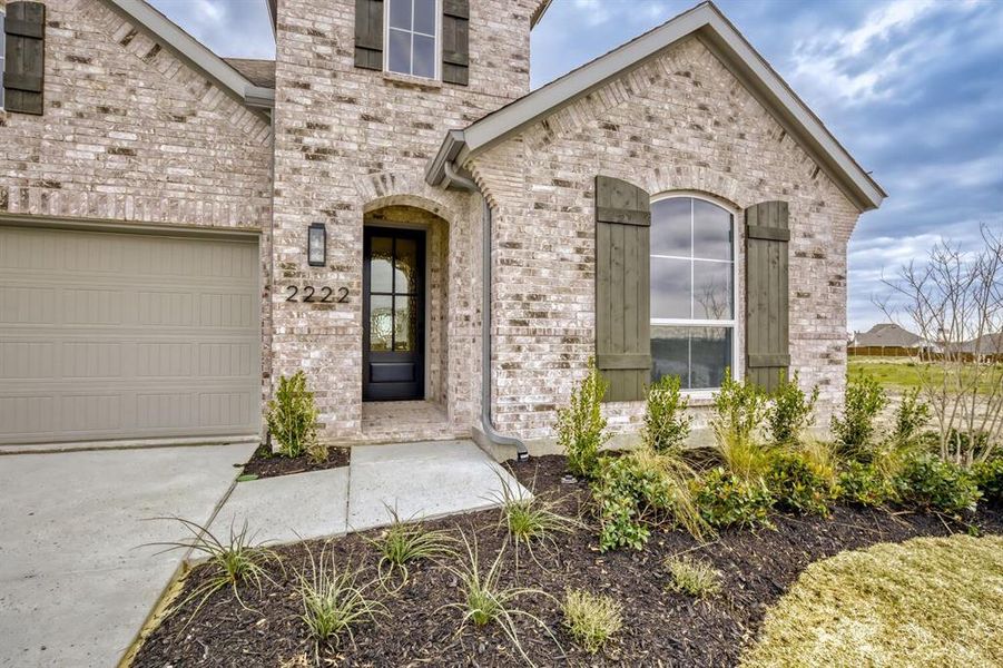 View of exterior entry featuring brick siding, a garage, and driveway