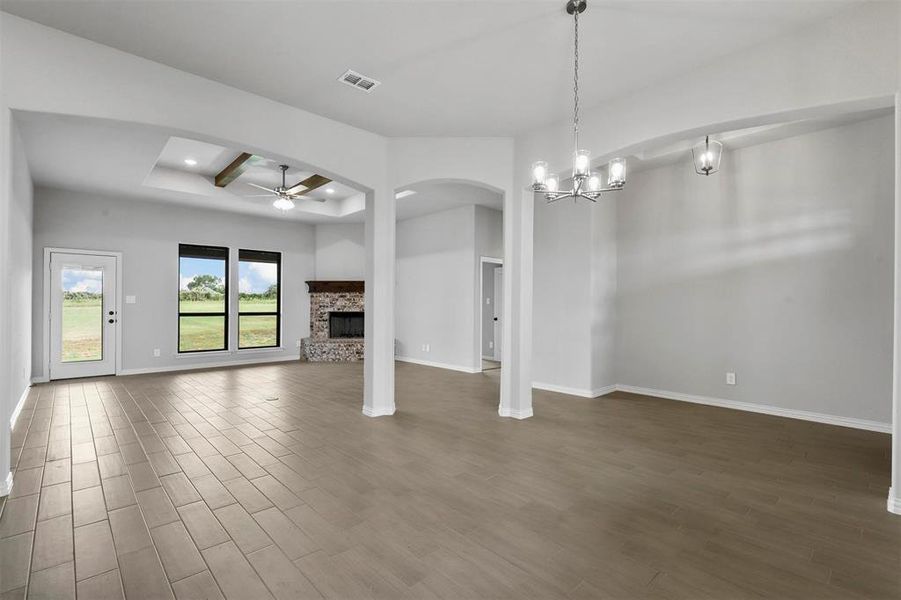 Unfurnished living room featuring a tray ceiling, ceiling fan with notable chandelier, wood-type flooring, and beam ceiling