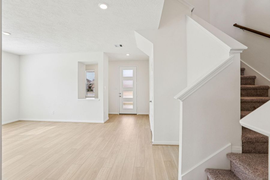 The entry features a modern front door with elegant glass inserts. A display shelf has been added to the Flex Room for convenience, while the staircase provides access to the upstairs game room, secondary bedrooms, and bathroom.