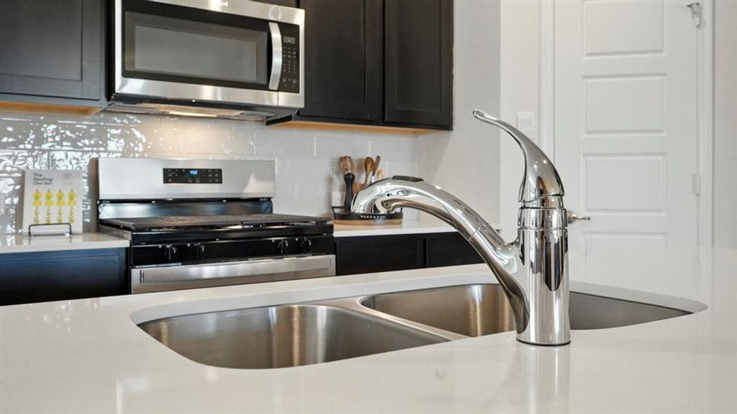 Kitchen featuring appliances with stainless steel finishes, backsplash, light stone countertops, and dark cabinetry
