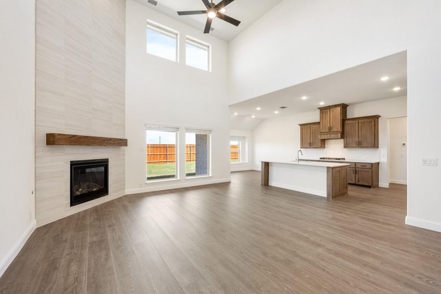 Open-concept living room with two-story ceiling, tile fireplace, and wood floors flowing into kitchen with island.