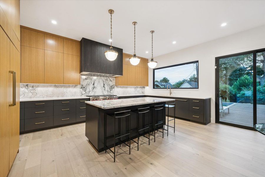 Kitchen featuring pendant lighting, modern cabinets, a breakfast bar, backsplash, and light stone countertops Kitchen featuring pendant lighting, modern cabinets, a breakfast bar, backsplash, and light stone countertops