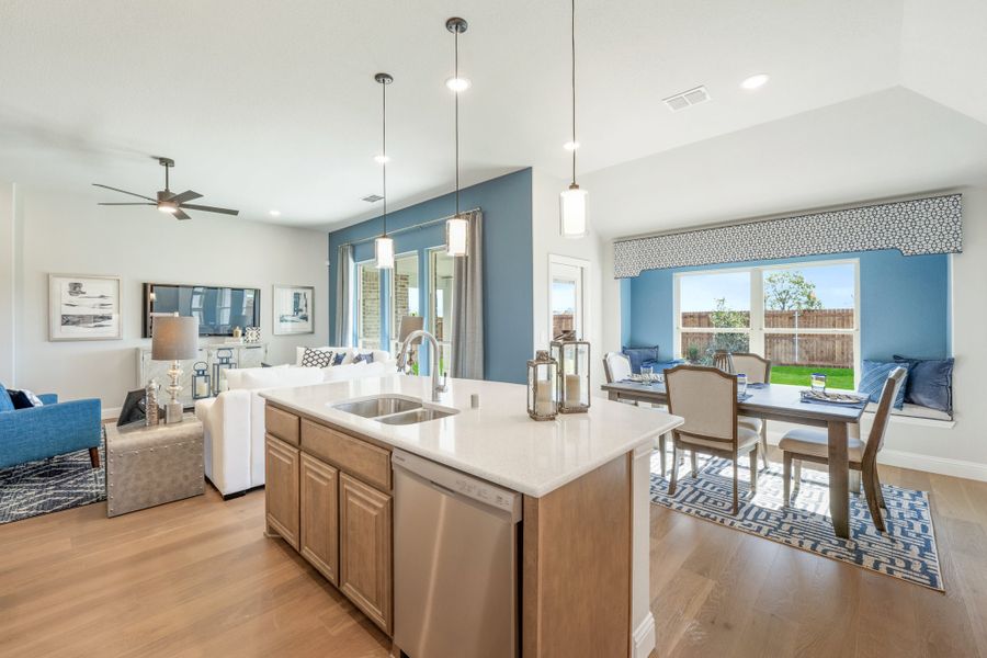 Open-concept kitchen with island, pendant lights, and views into dining and living areas with hardwood floors