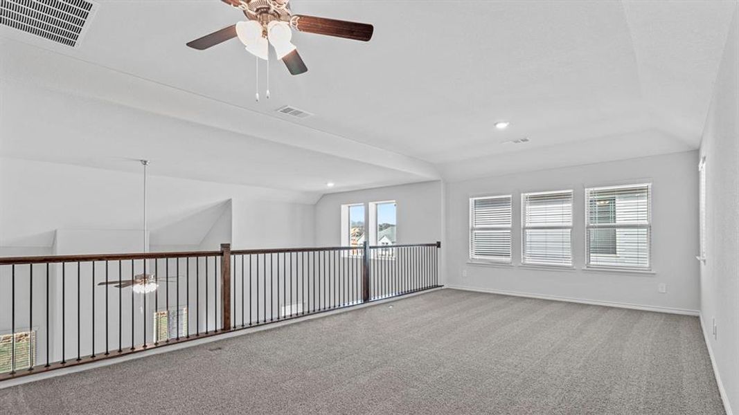 Spacious loft area featuring neutral-toned carpet, a ceiling fan, and multiple windows with blinds