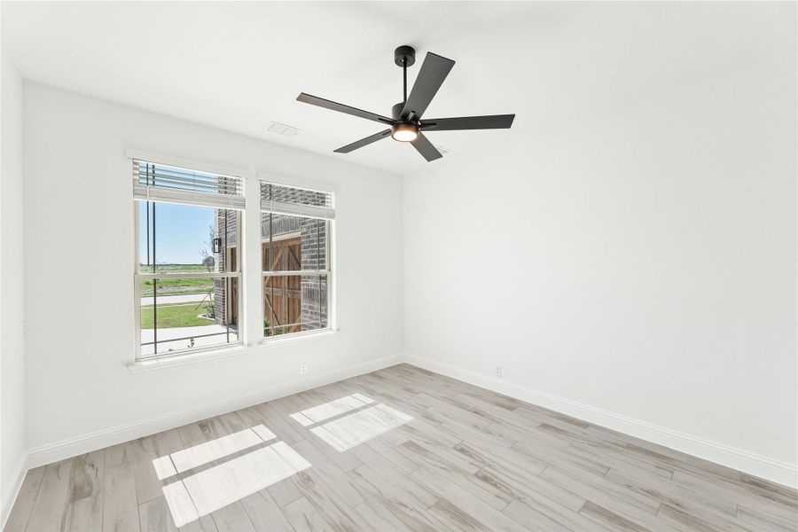Empty bedroom with light wood floors, black ceiling fan, and large window with outdoor view Empty bedroom with light wood floors, black ceiling fan, and large window with outdoor view
