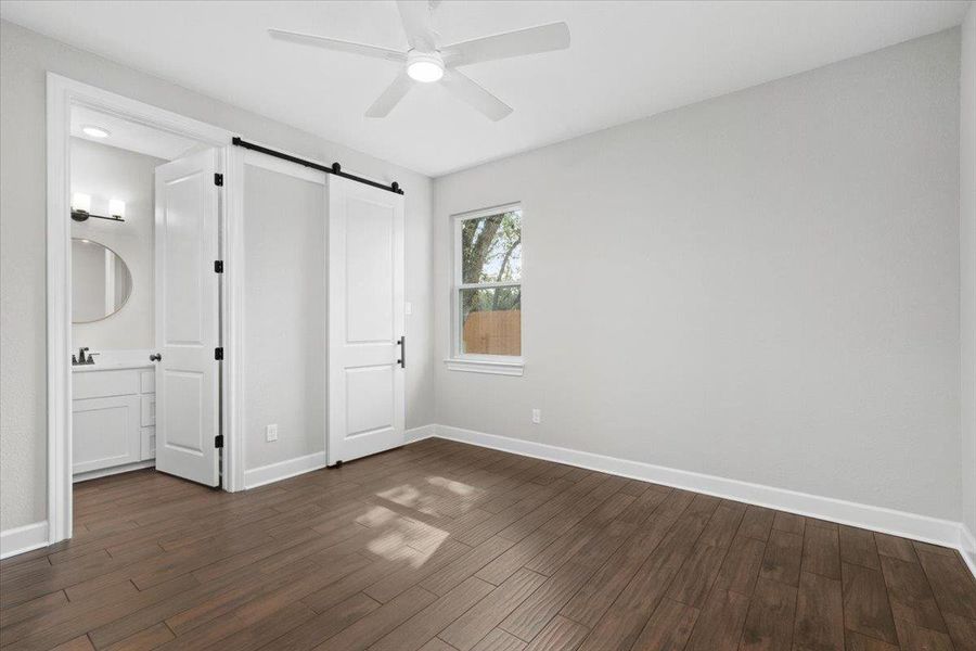 Unfurnished bedroom with a barn door, dark wood-style floors, baseboards, and ceiling fan Unfurnished bedroom with a barn door, dark wood-style floors, baseboards, and ceiling fan