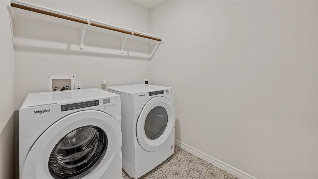 Utility area featuring a patterned tile floor, a built-in shelf with a hanging rod, and white baseboards Utility area featuring a patterned tile floor, a built-in shelf with a hanging rod, and white baseboards