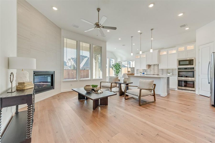 Living room with ceiling fan, a tiled fireplace, and light hardwood / wood-style floors