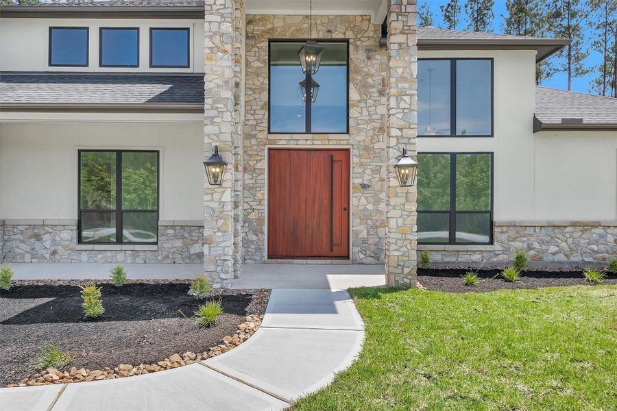The grand entrance showcases a rich wooden door framed by a striking stone facade, tall windows, and elegant lantern lighting for a sophisticated welcome. The grand entrance showcases a rich wooden door framed by a striking stone facade, tall windows, and elegant lantern lighting for a sophisticated welcome.