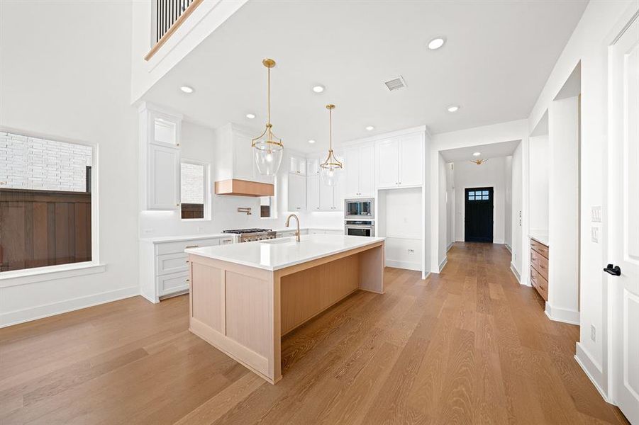 Kitchen featuring a kitchen island with sink, white cabinetry, pendant lighting, light wood-type flooring, and recessed lighting Kitchen featuring a kitchen island with sink, white cabinetry, pendant lighting, light wood-type flooring, and recessed lighting