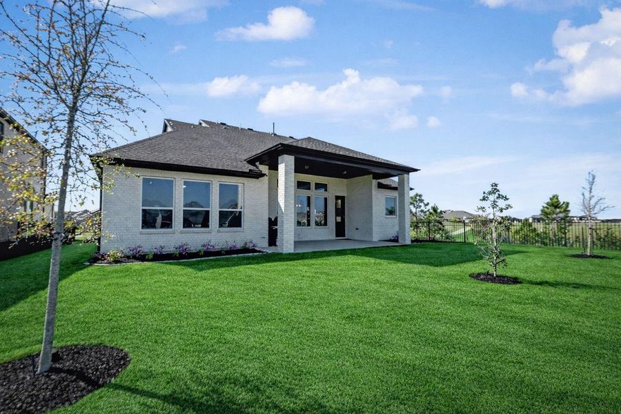 The rear of the home features white brick construction and a deep covered porch supported by a substantial brick pillar. Large windows provide plenty of natural light to the interior living spaces while overlooking the green space.