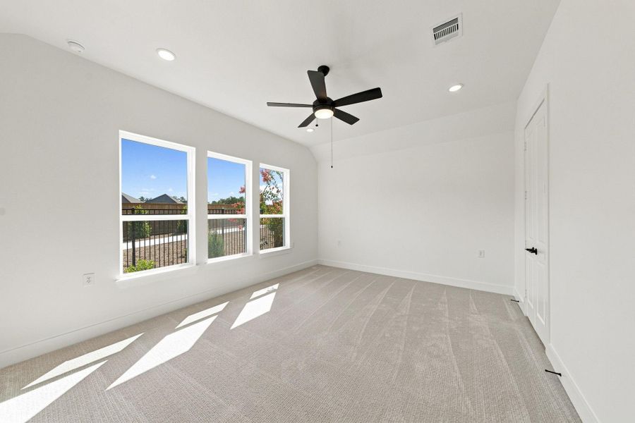 Private primary suite with a vaulted ceiling, ceiling fan, recessed lighting, and three large windows providing abundant natural light.