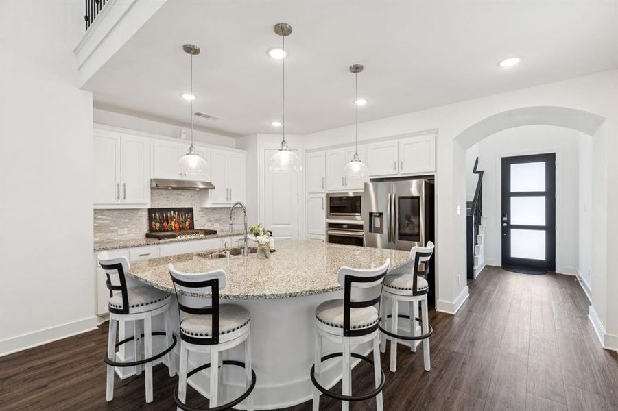 Kitchen with white cabinetry, arched walkways, pendant lighting, a kitchen breakfast bar, and decorative backsplash Kitchen with white cabinetry, arched walkways, pendant lighting, a kitchen breakfast bar, and decorative backsplash