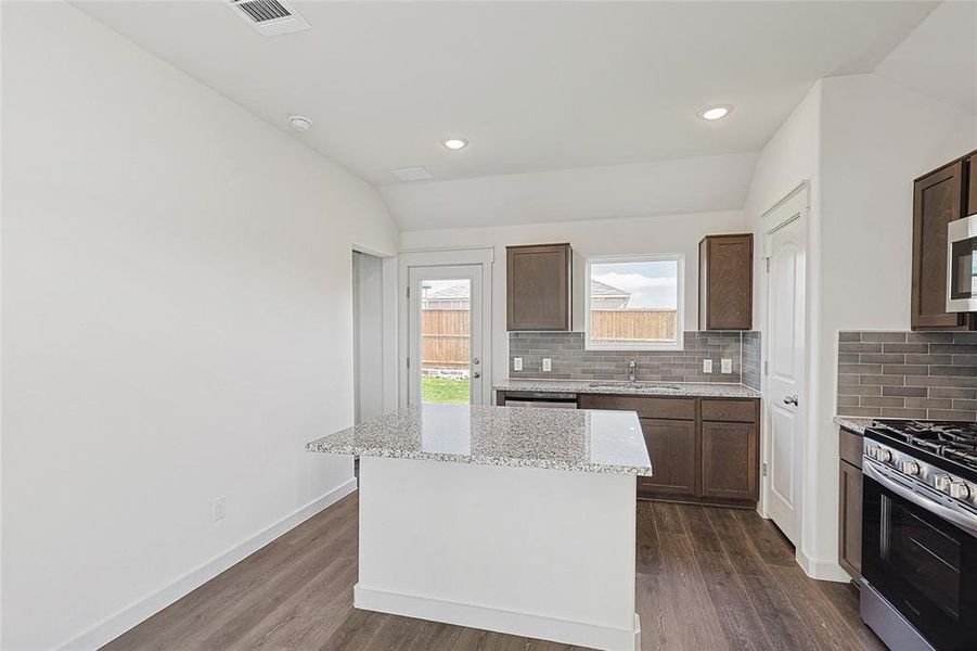 Kitchen featuring sink, a kitchen island, vaulted ceiling, dark wood-type flooring, and gas range