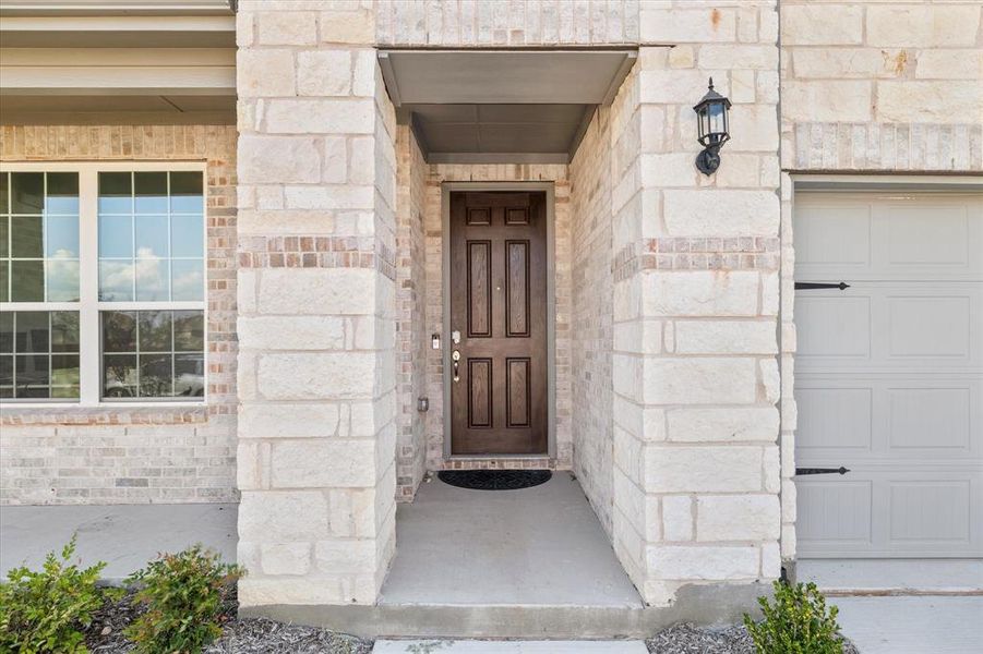 Exterior facade featuring a wood-finish entry door, stone and brick accents, a covered porch, and an attached garage with decorative hardware