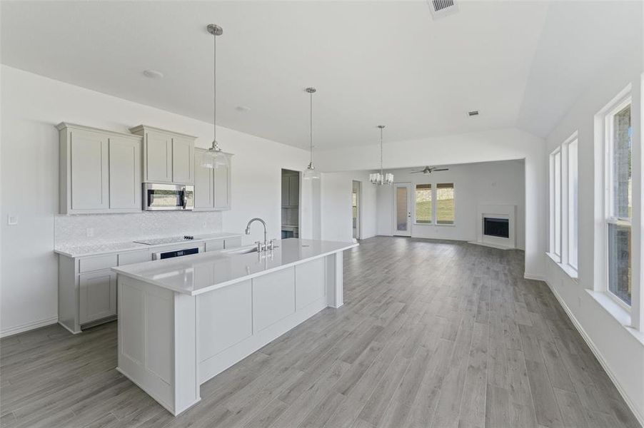 Kitchen featuring stainless steel microwave, a kitchen island with sink, a fireplace, and pendant lighting