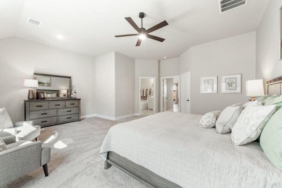 Spacious master bedroom with vaulted ceiling, ceiling fan, carpet flooring, and ensuite bathroom doorway visible.