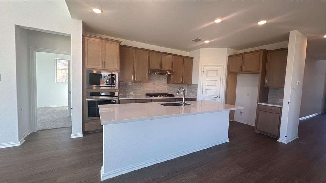 Kitchen featuring backsplash, appliances with stainless steel finishes, dark wood finished floors, a kitchen island with sink, and recessed lighting