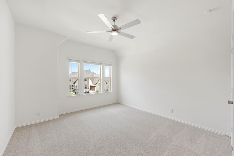 Empty bedroom with vaulted ceiling, ceiling fan, carpet flooring, and triple window with neighborhood view Empty bedroom with vaulted ceiling, ceiling fan, carpet flooring, and triple window with neighborhood view