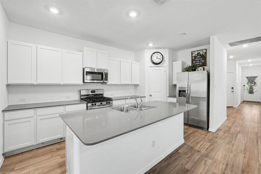 Kitchen featuring a central island with an integrated double basin sink, light grey countertops, and ample white cabinetry