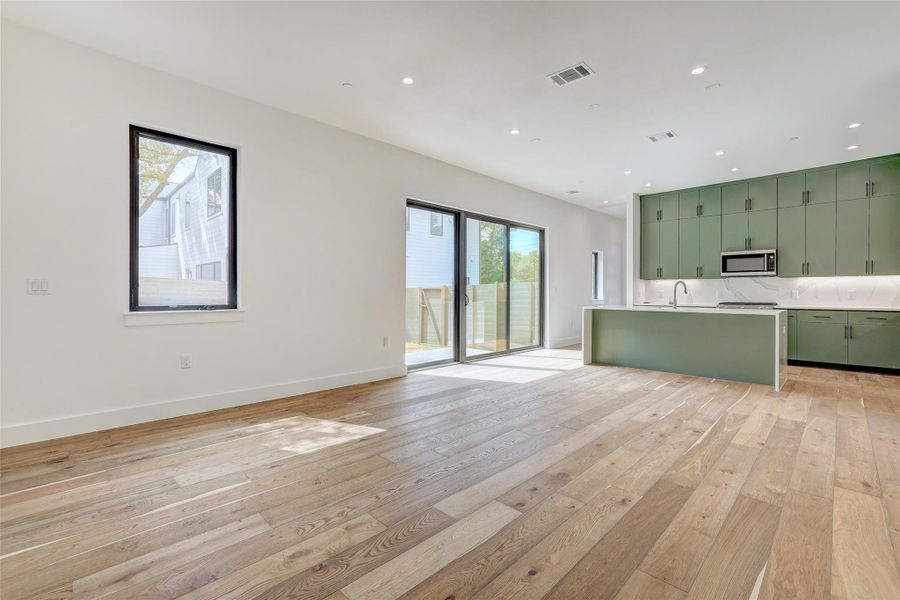 Kitchen with green cabinets, light wood-type flooring, light countertops, stainless steel microwave, and open floor plan