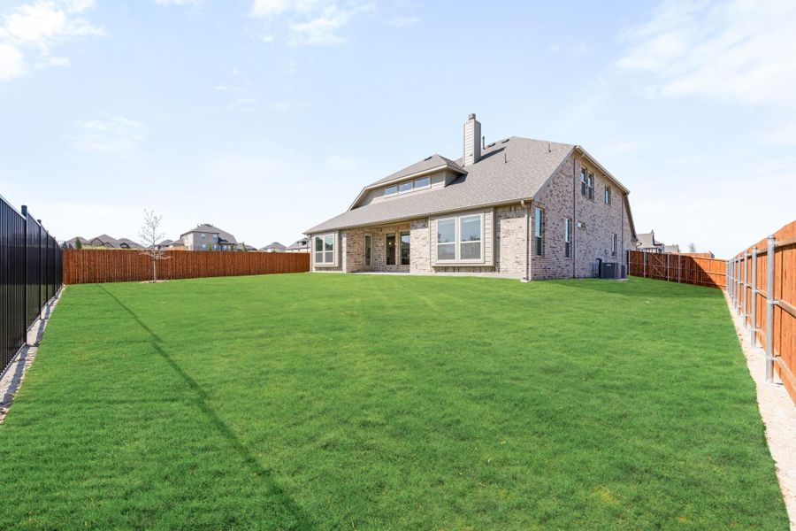 Backyard of two-story brick home with large green lawn and wood privacy fence