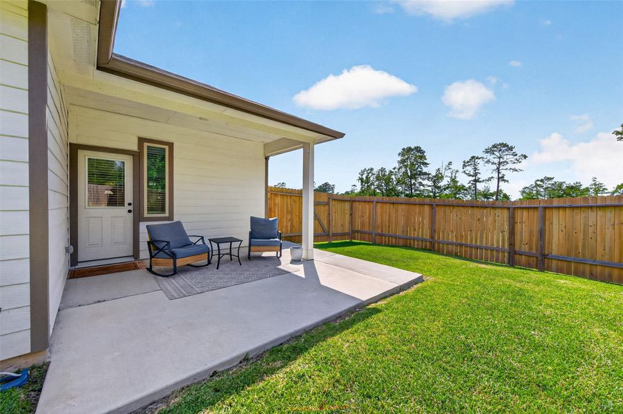 This photo shows a cozy backyard patio with comfortable seating, a small table, and a well-maintained lawn. It's enclosed by a wooden fence, providing privacy and a serene view of surrounding trees. This photo shows a cozy backyard patio with comfortable seating, a small table, and a well-maintained lawn. It's enclosed by a wooden fence, providing privacy and a serene view of surrounding trees.