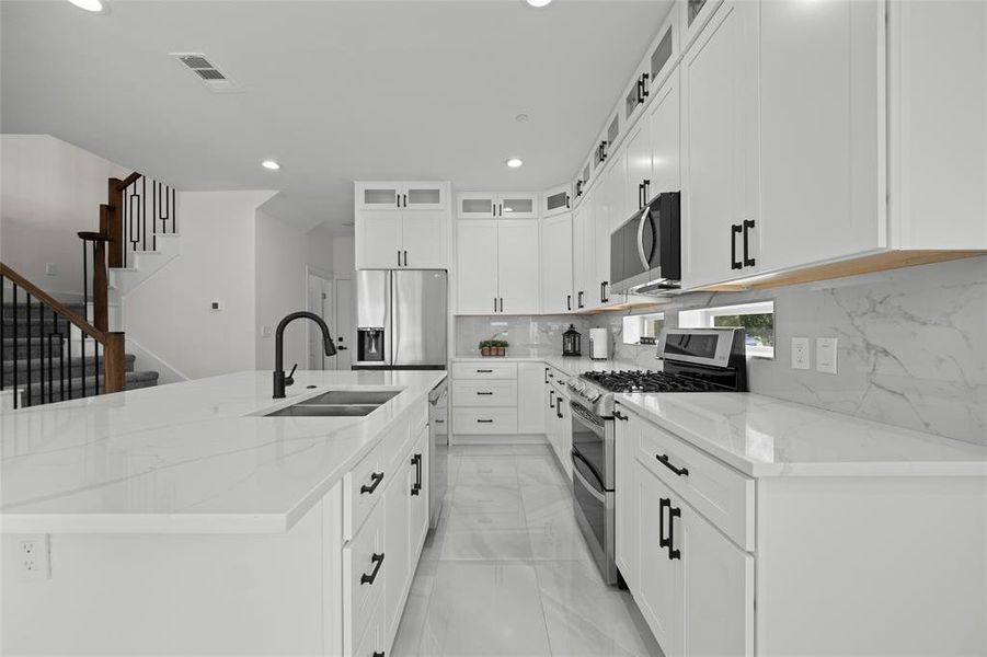 Kitchen with an island with sink, appliances with stainless steel finishes, sink, and white cabinetry