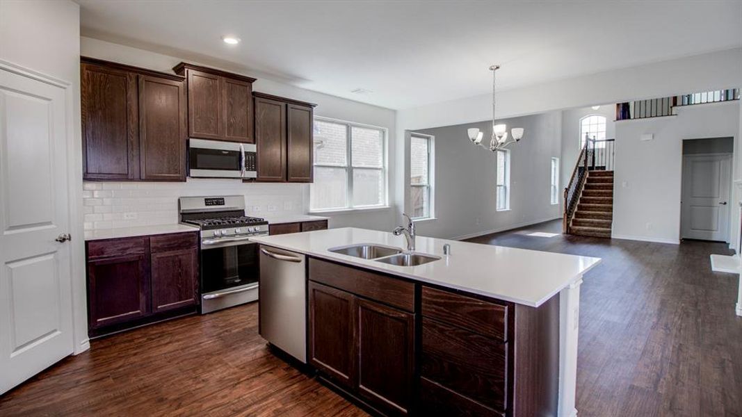 Kitchen featuring appliances with stainless steel finishes, dark brown cabinets, dark wood-style flooring, a kitchen island with sink, and recessed lighting Kitchen featuring appliances with stainless steel finishes, dark brown cabinets, dark wood-style flooring, a kitchen island with sink, and recessed lighting