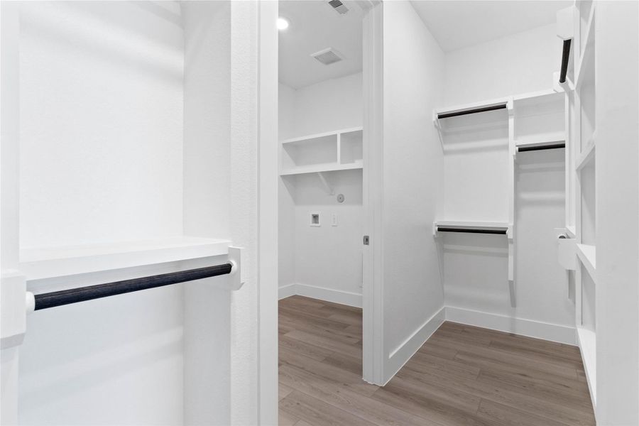 The spacious walk-in closet is equipped with clean white shelving and sturdy matte black hanging rods, offering extensive solutions for organizing an entire wardrobe. This closet also features direct access to the laundry room, a dream feature for modern living. The spacious walk-in closet is equipped with clean white shelving and sturdy matte black hanging rods, offering extensive solutions for organizing an entire wardrobe. This closet also features direct access to the laundry room, a dream feature for modern living.