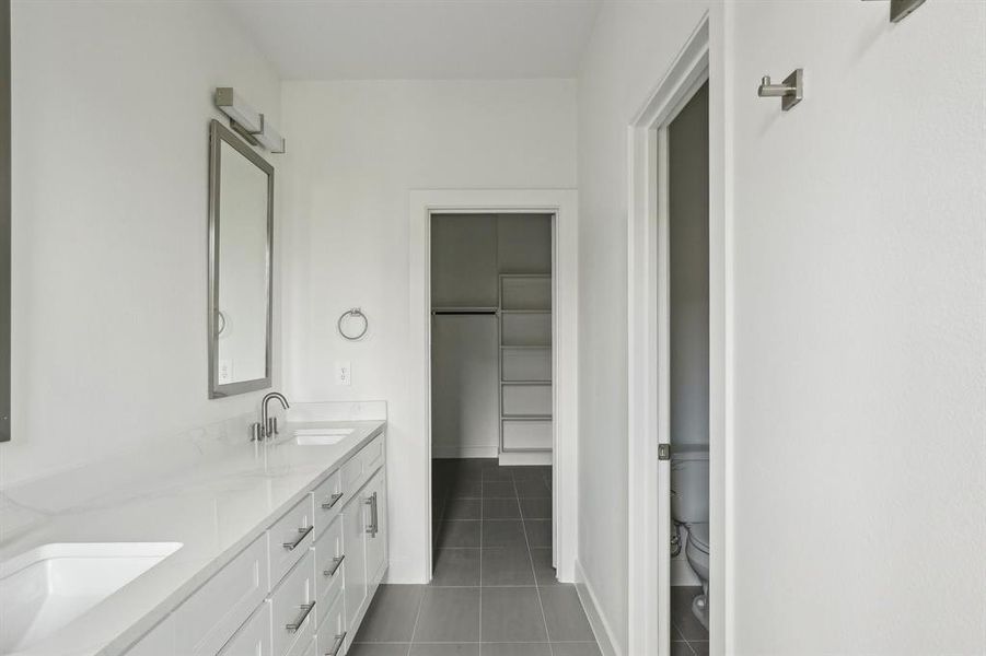 Bathroom featuring tile patterned flooring, toilet, double vanity, a walk in closet, and baseboards