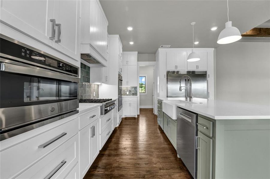 Kitchen with a tiled fireplace, beamed ceiling, dark wood-type flooring, a kitchen island with sink, and appliances with stainless steel finishes