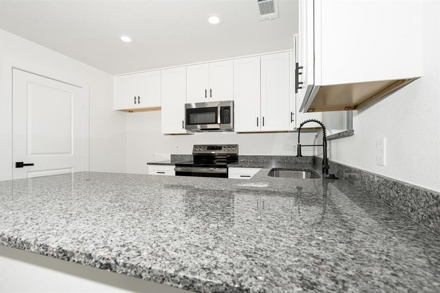 Kitchen with dark stone counters, a peninsula, stainless steel appliances, white cabinetry, and recessed lighting