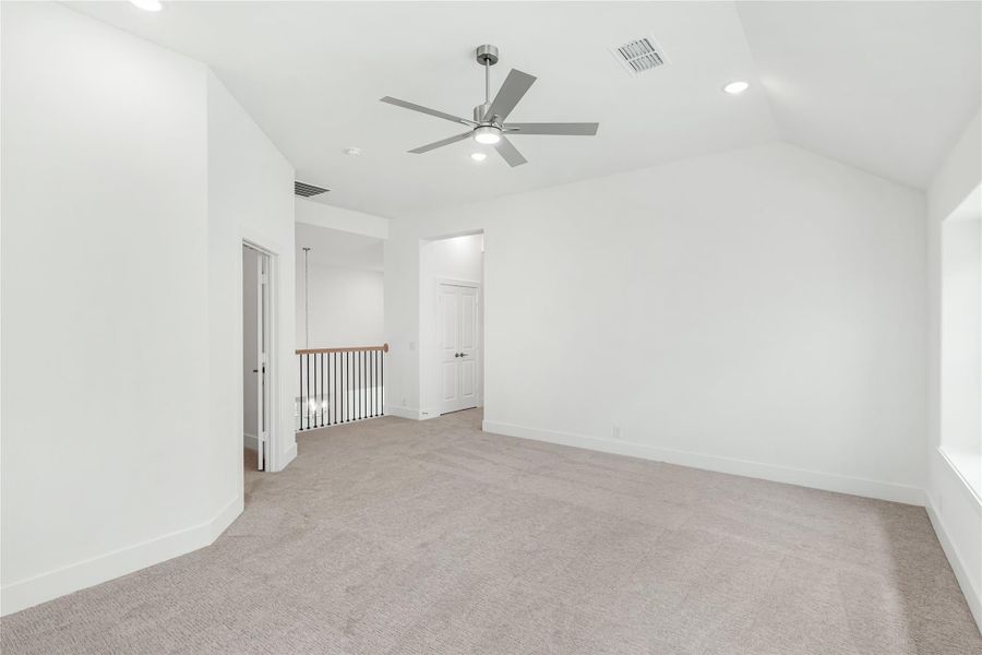 Empty room with vaulted ceiling, ceiling fan, carpet flooring, and staircase railing visible in background