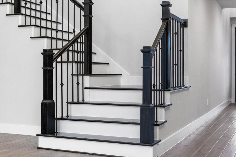 This sophisticated modern-transitional staircase features a bold contrast of crisp white risers and deep black treads, elegantly framed by traditional black-stained newel posts and slender wrought-iron balusters.