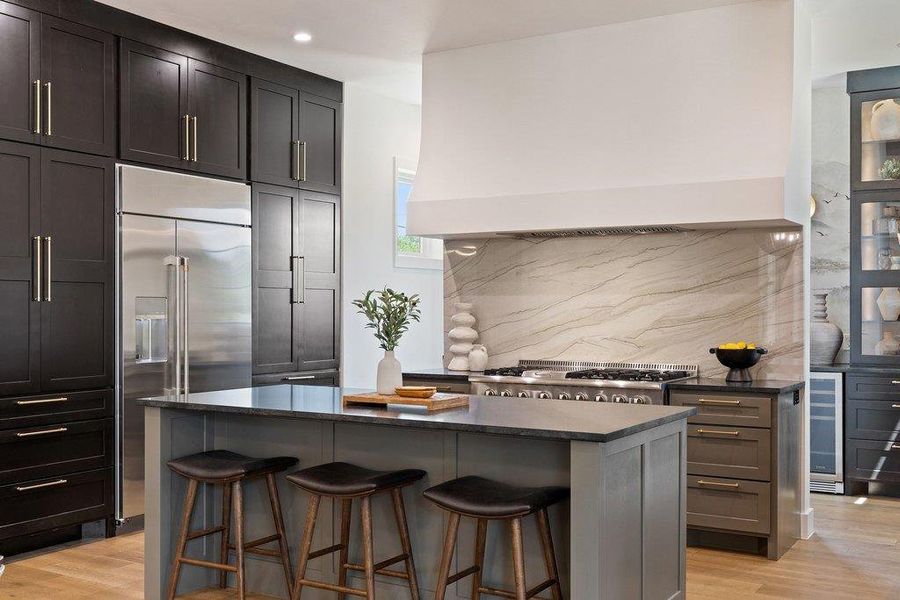 A grand chef's kitchen features a central island with bar seating, full-height cabinetry, and modern stainless steel appliances.