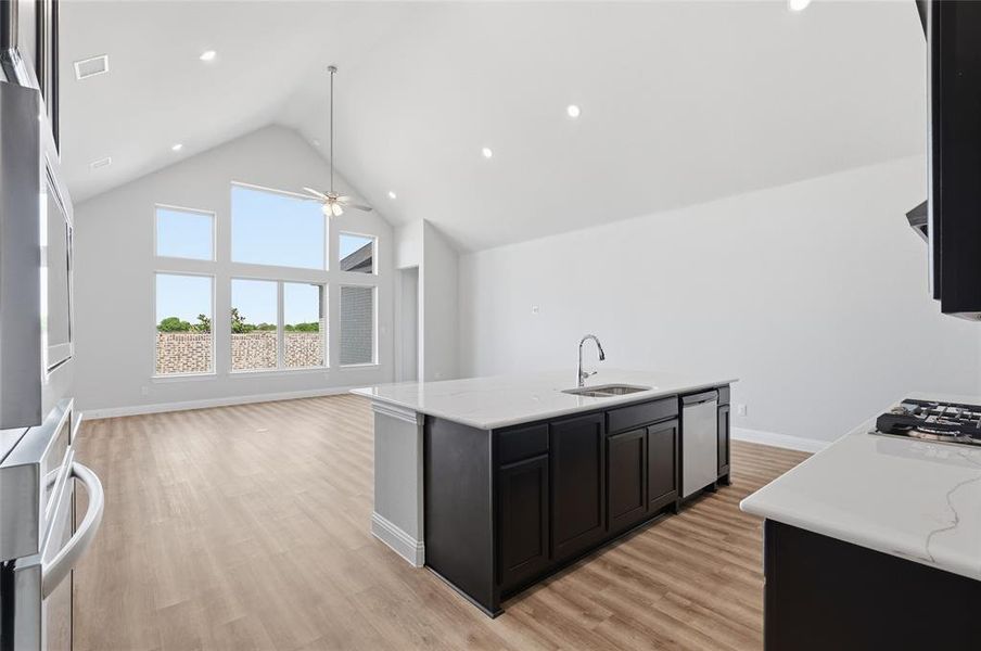 Kitchen with a high ceiling, dark cabinets, open floor plan, a center island with sink, and light wood-style flooring Kitchen with a high ceiling, dark cabinets, open floor plan, a center island with sink, and light wood-style flooring