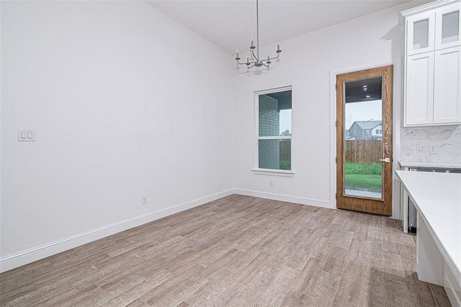 Unfurnished dining area with a chandelier, light wood finished floors, lofted ceiling, and baseboards Unfurnished dining area with a chandelier, light wood finished floors, lofted ceiling, and baseboards