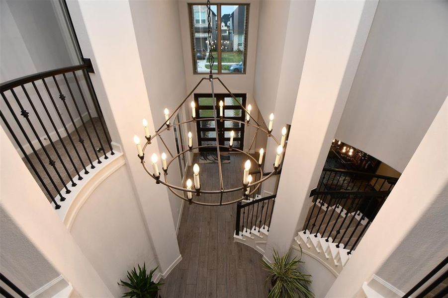 This photo showcases a grand entryway with high ceilings and a large, elegant chandelier. It features a stylish staircase with modern black railings and light wood flooring, creating an inviting and spacious atmosphere.